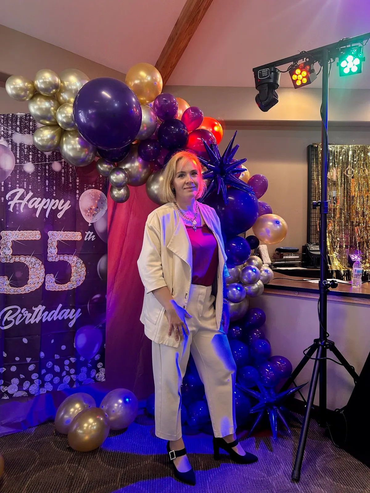 Host by the Happy 55th Birthday balloon backdrop at a family party