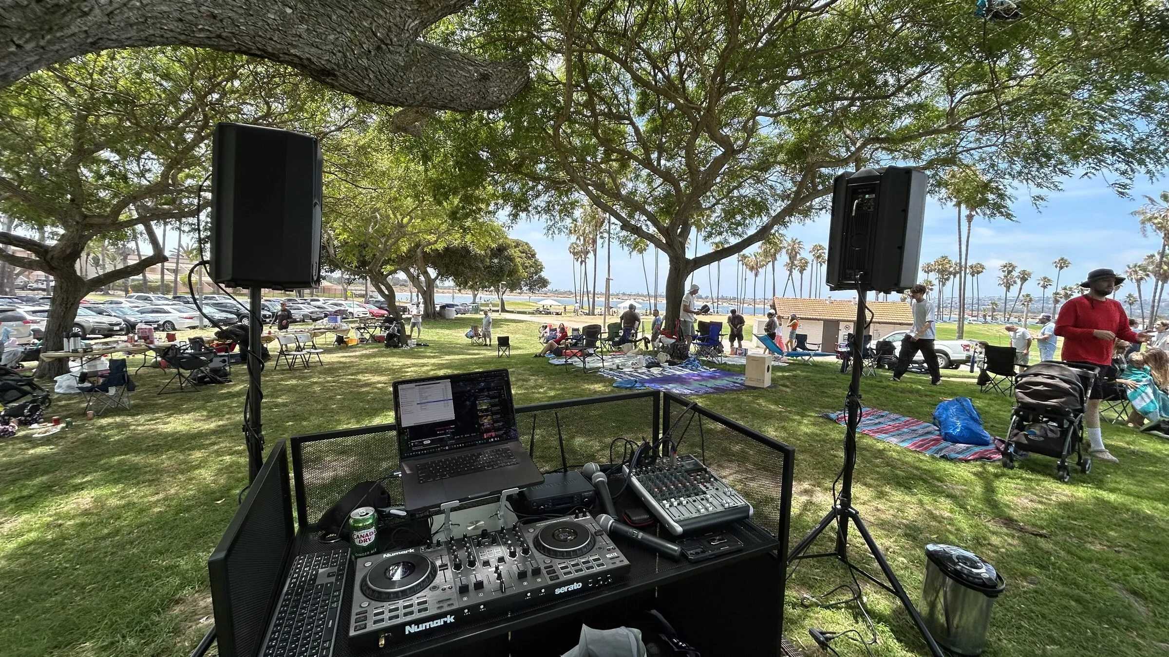 Outdoor DJ setup in a San Diego park — booth, controller and speakers on stands with the bay and palms behind