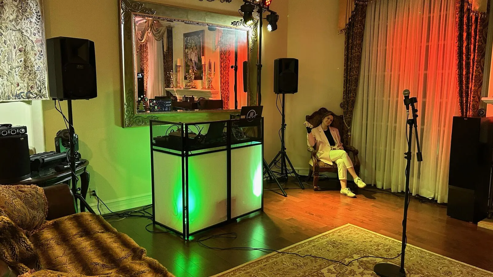 Lit DJ booth, speakers, stage lights and a microphone stand set up in a living room for a house party