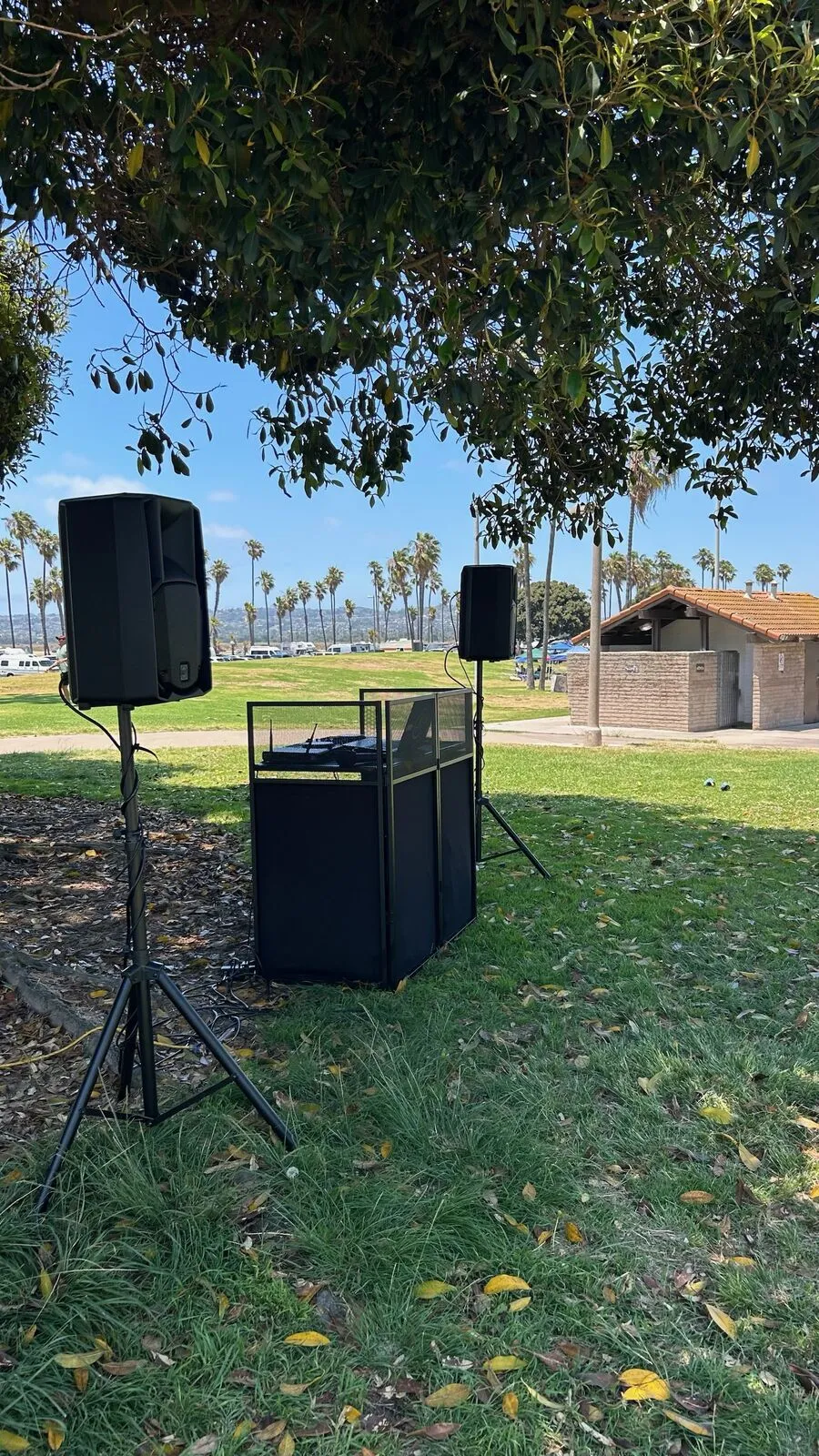 DJ booth and speakers on stands on the grass in a park by Mission Bay, San Diego, palms and the bay behind