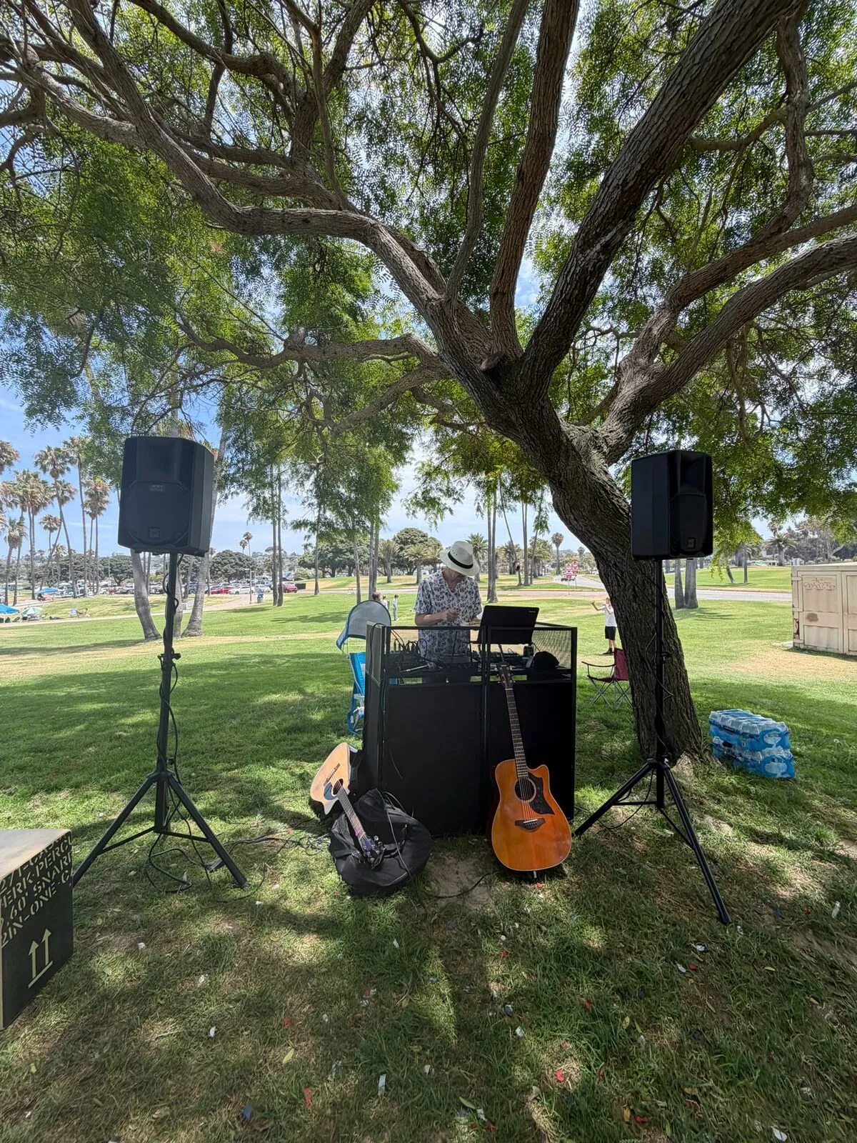 DJ booth and speakers under a tree in a park by Mission Bay, San Diego, acoustic guitars beside the booth